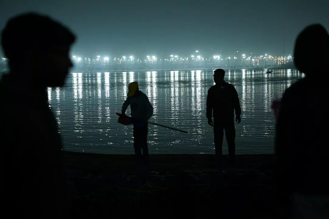 People stand by a river at night with lights reflecting